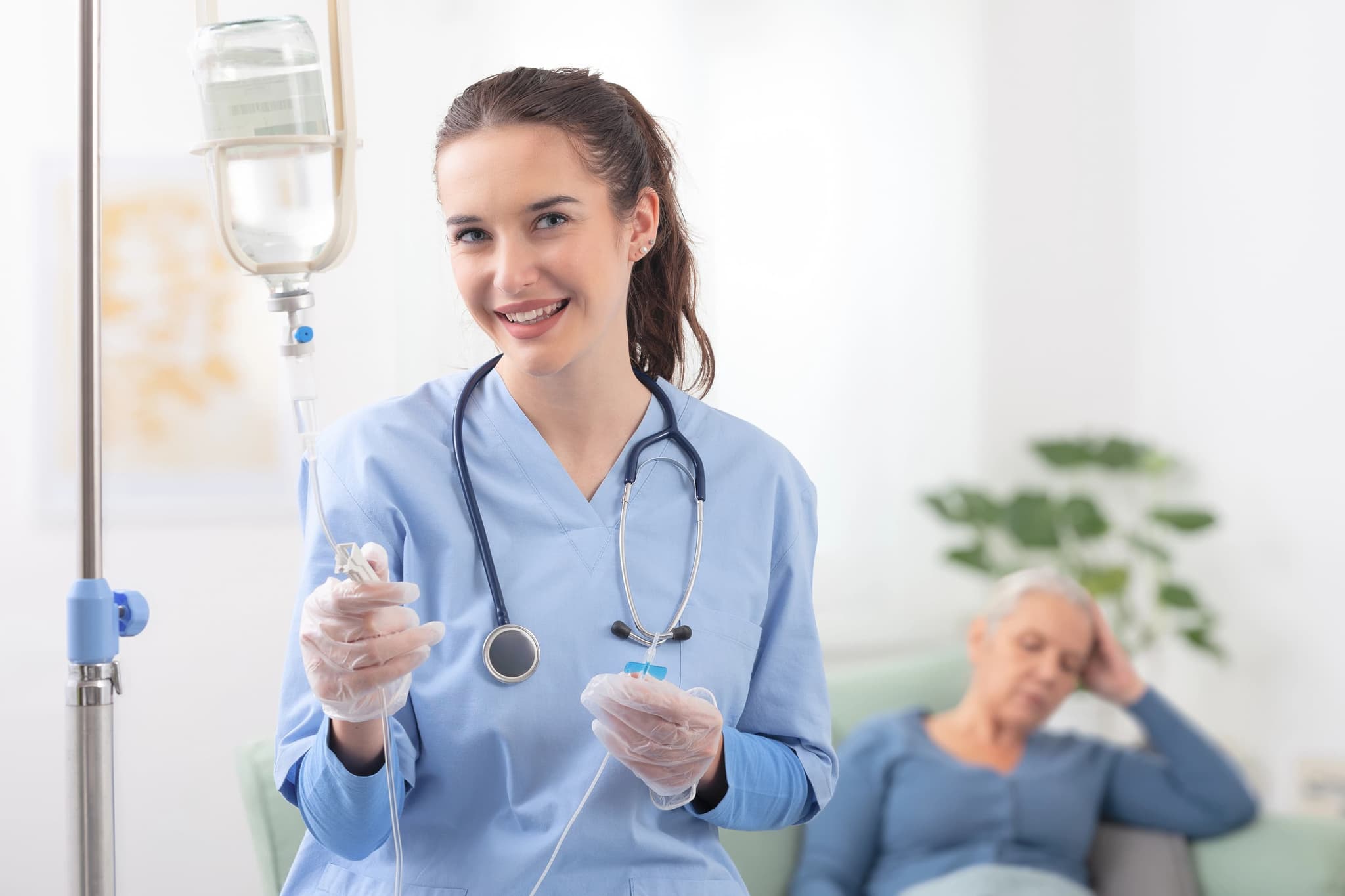 Nurse smiling while preparing an IV drip for a woman resting on a couch during at-home IV therapy.